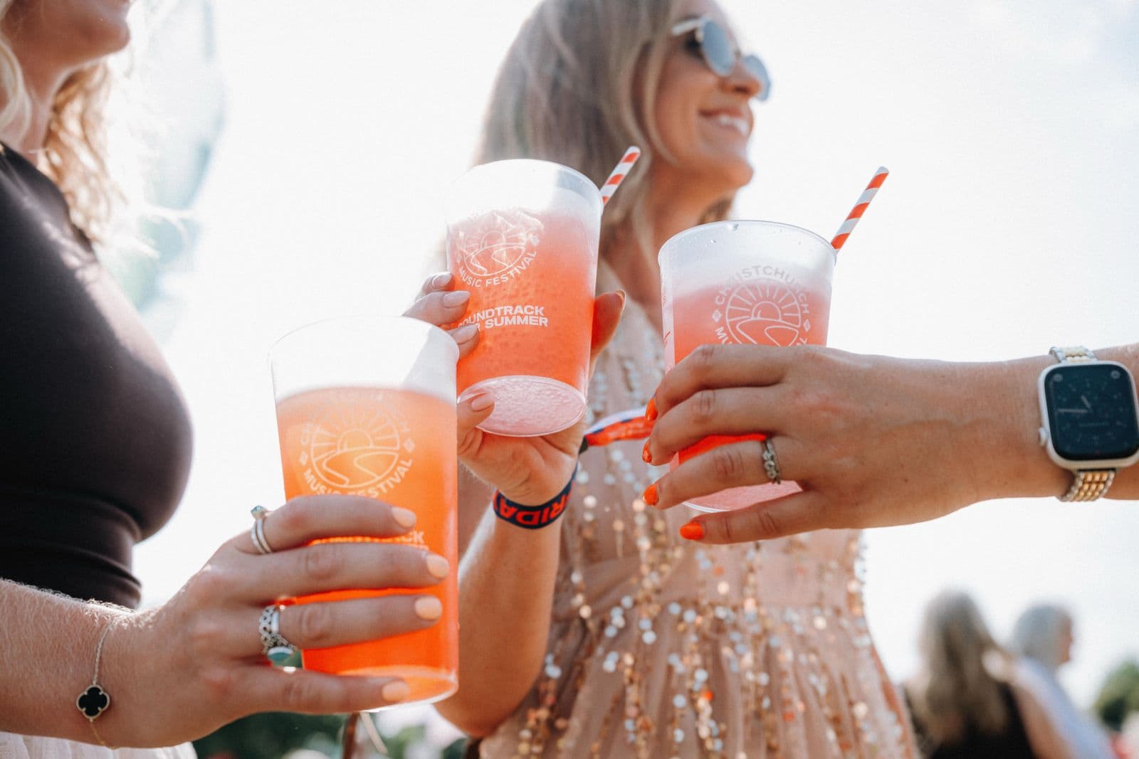 Three friends toasting with printed reusable festival cups at Christchurch Music Festival